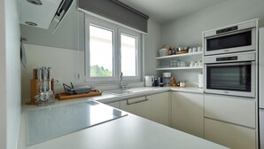 Cozinha moderna com armários brancos, uma pia dupla e dois fornos embutidos.