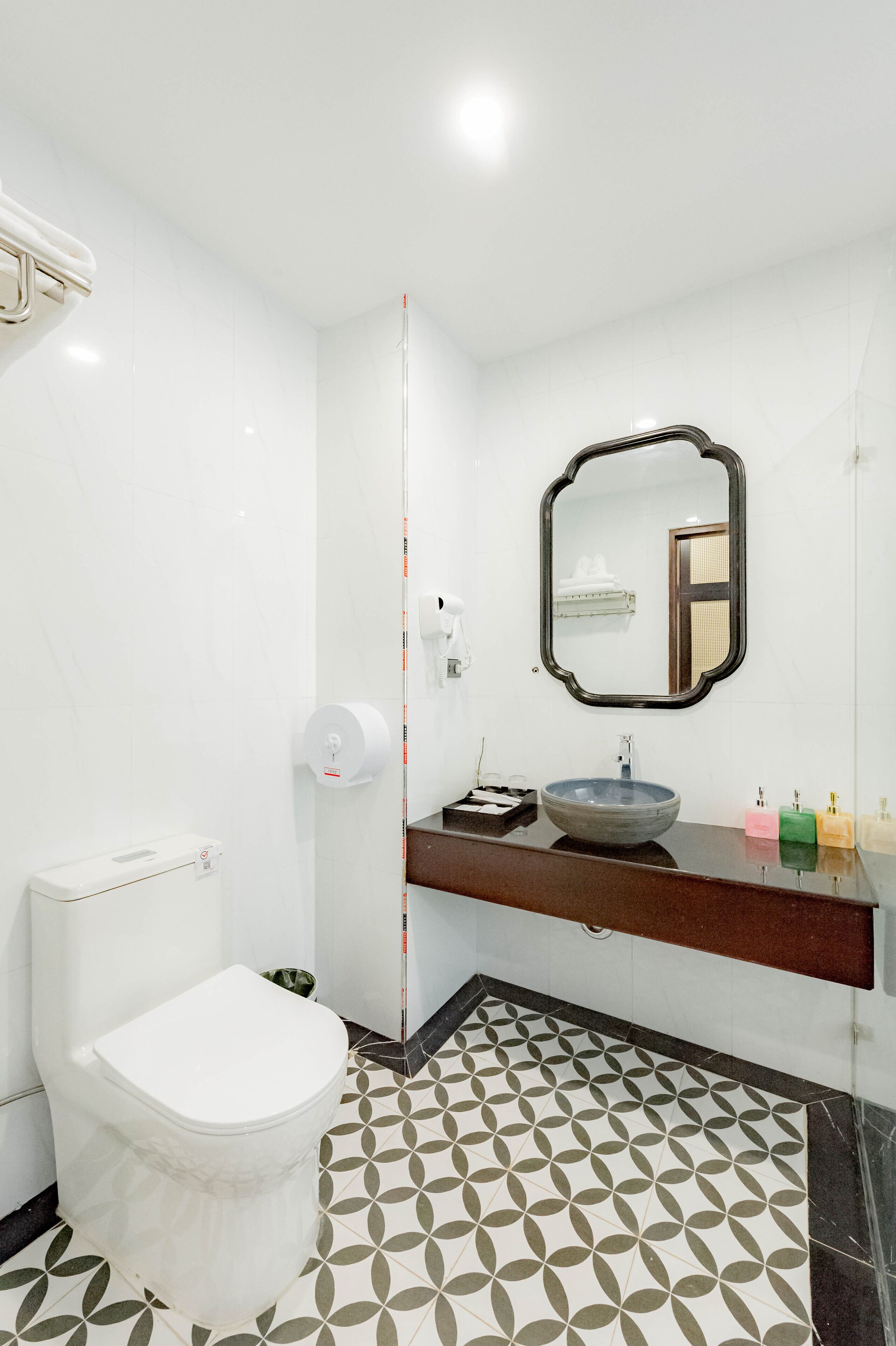 Ein Badezimmer mit einer weißen Toilette, einem Waschbecken mit Spiegel darüber und fugenreichen Bodenfliesen.