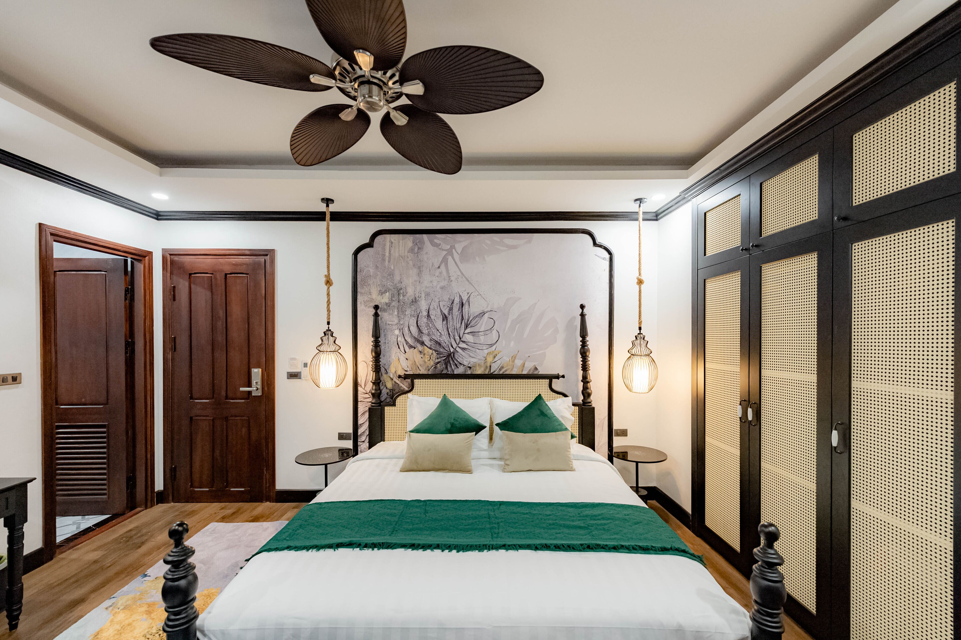 A bedroom with a large bed, a ceiling fan, wooden doors, and a wall-mounted light fixture.