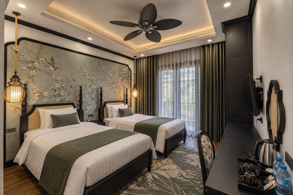 A hotel room with two beds, a ceiling fan, a wall-mounted TV, and a window with curtains.