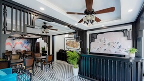 Un restaurant moderne avec un sol à motifs en noir et blanc, des ventilateurs de plafond en bois et différents types de sièges, notamment des tables et des chaises.