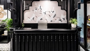 Un espace d’accueil doté d’un comptoir noir, d’un ventilateur de plafond et d’un mur orné d’une fresque représentant des oiseaux.