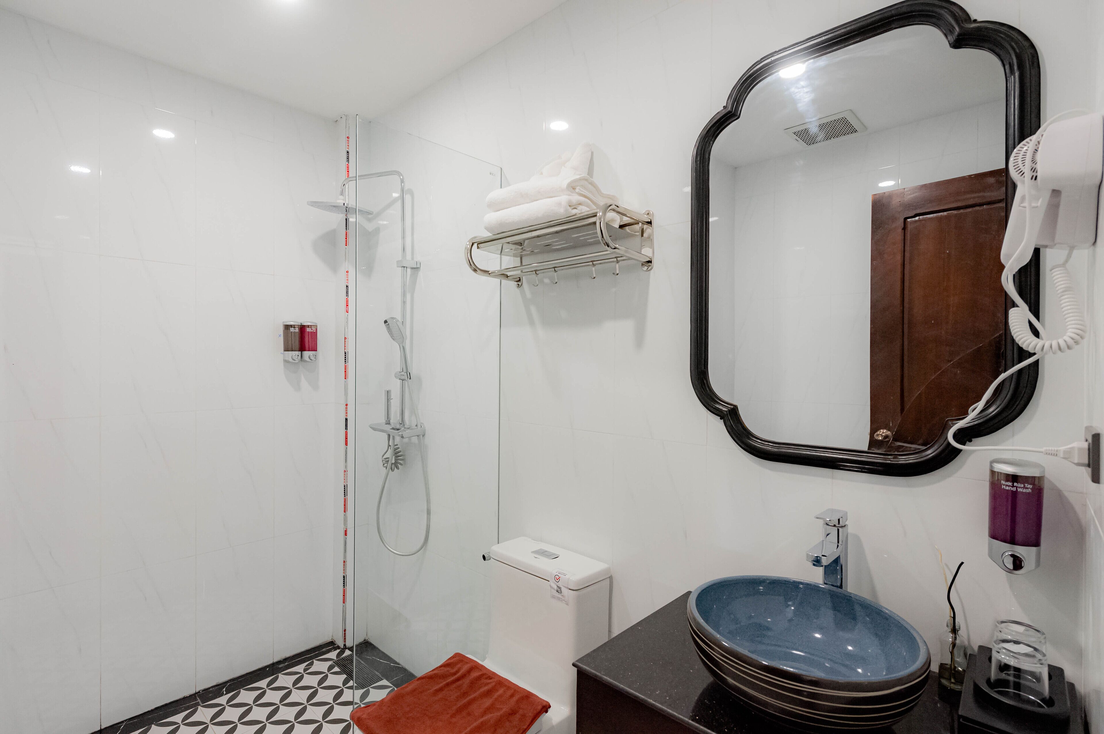 A modern bathroom with a glass-enclosed shower, a white toilet, a sink with a blue basin, and a large mirror.