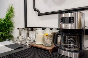 A coffee maker with a digital display, a milk frother, and two glass containers with tea bags on a wooden tray. - Palm Golden Luangprabang Hotel (Luang Prabang)