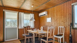 A cozy cabin interior with a wooden ceiling, a dining table with chairs, an air conditioning unit, and a window with curtains. - 2 bedroom stunning home in Vordingborg (Vordingborg)