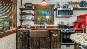 Una cocina con armarios de madera, un lavamanos, una estufa, un microondas y una ventana con persianas.