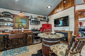 A rustic kitchen with wooden cabinets, a stove, a microwave, and a red coffee machine. - Rockin' R - Morning Star Cabin (Fredericksburg)