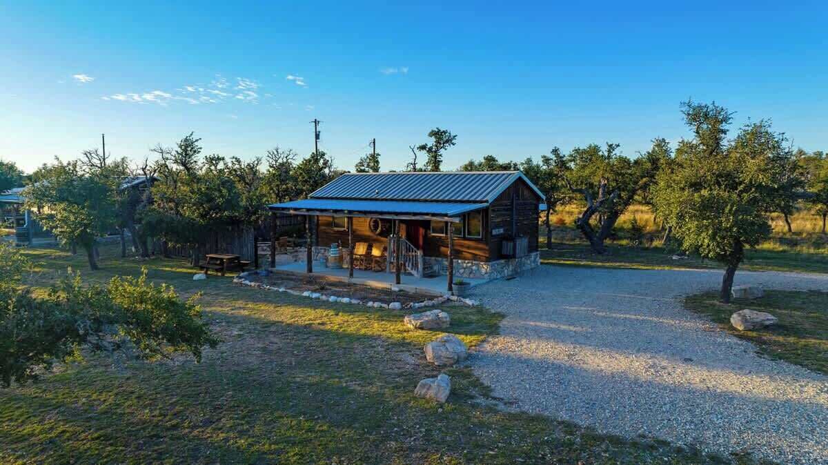 Un chalet rustique avec un toit en métal, entouré d’arbres et bordé d’un chemin de gravier.