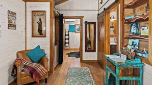 A cabin interior with a leather armchair, a small table, wooden walls, and a ceiling with a metal roof. - Rockin' R - Rustic Star Cabin (Fredericksburg)