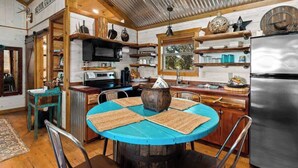 A rustic kitchen with wooden shelves, a round table with placemats, a refrigerator, and a sign reading 'OUR GUEST'. - Rockin' R - Rustic Star Cabin (Fredericksburg)