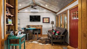 A rustic interior with a wooden ceiling, a red door, a desk with a computer, a leather couch, and a cowhide rug. - Rockin' R - Rustic Star Cabin (Fredericksburg)