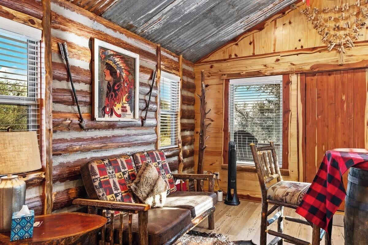 En stuga byggd av timmer med en soffa, stolar, ett bord och ett fönster med persienner.