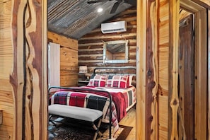 Camera da letto in una baita di legno con un letto, una panca, uno specchio e un condizionatore d'aria.