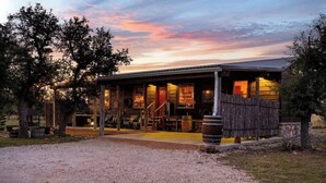 A rustic building with a porch, a covered outdoor seating area, and a gravel driveway. - Rockin' R - Mason Jar Cabin (Fredericksburg)