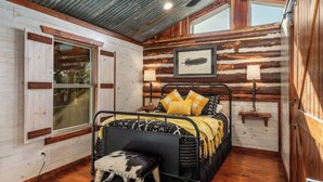 A rustic cabin bedroom with a metal bed, wooden walls, a ceiling fan, and a window. - Rockin' R - Mason Jar Cabin (Fredericksburg)
