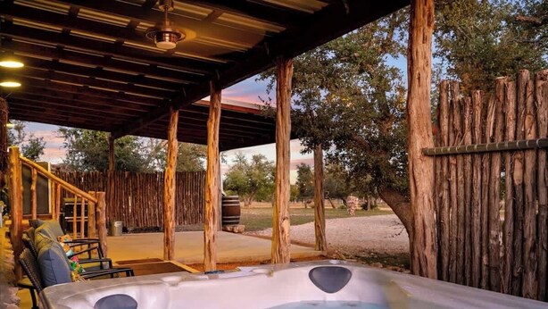 A hot tub under a wooden pergola with a view of trees and a gravel path. - Rockin' R - Mason Jar Cabin (Fredericksburg)