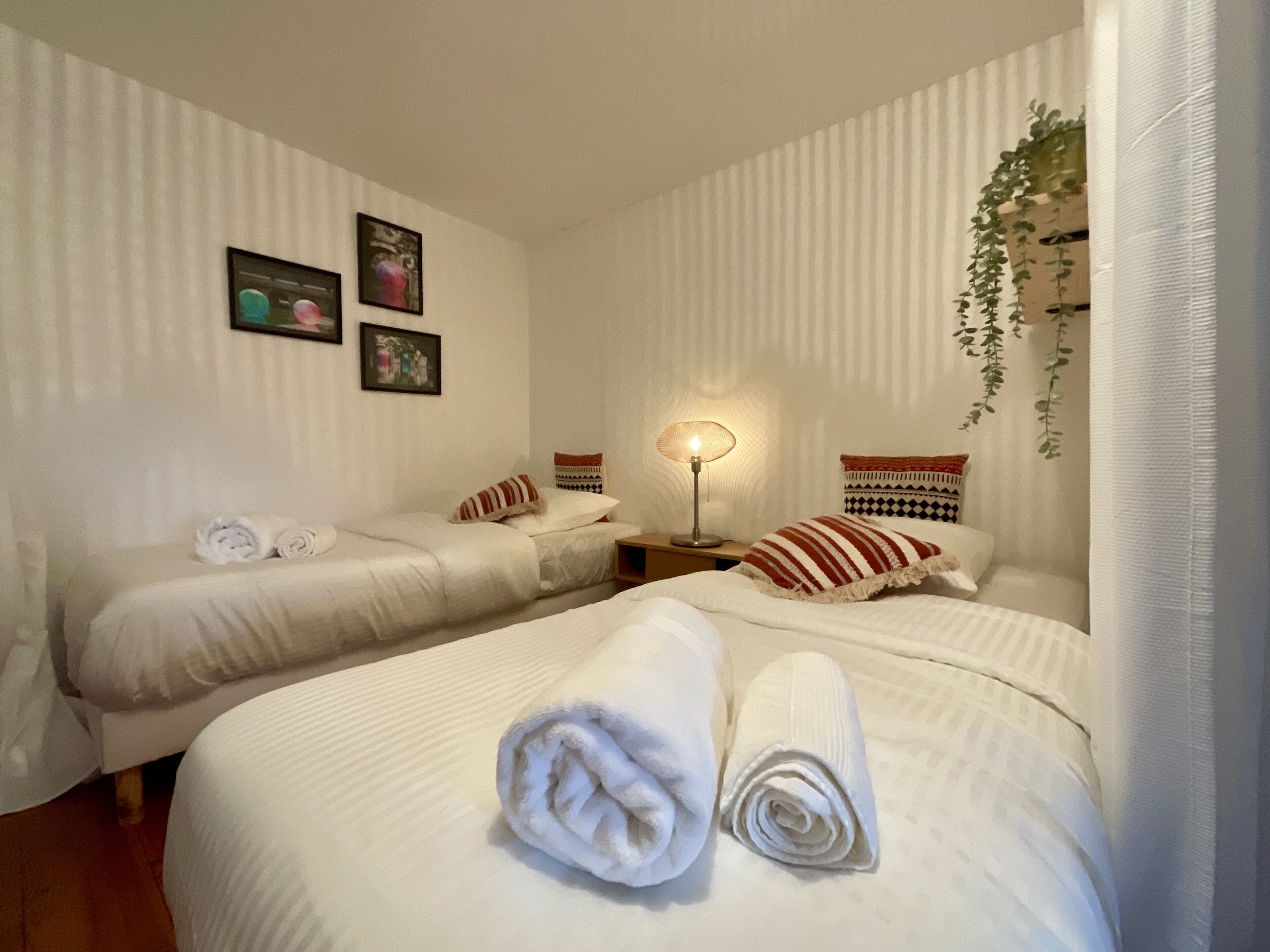 Een hotelkamer met twee eenpersoonsbedden, een nachtkastje met een lamp, een hangende plant en een muur met ingelijste foto's.
