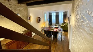 A staircase leading to a living area with a dining table, a green sofa, and a television in the background. - Distinguished Townhouse, "L'Aparté" (Verdun)