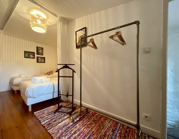 A hotel room with two beds, a hanging clothes rack, a patterned rug, and a ceiling light fixture.