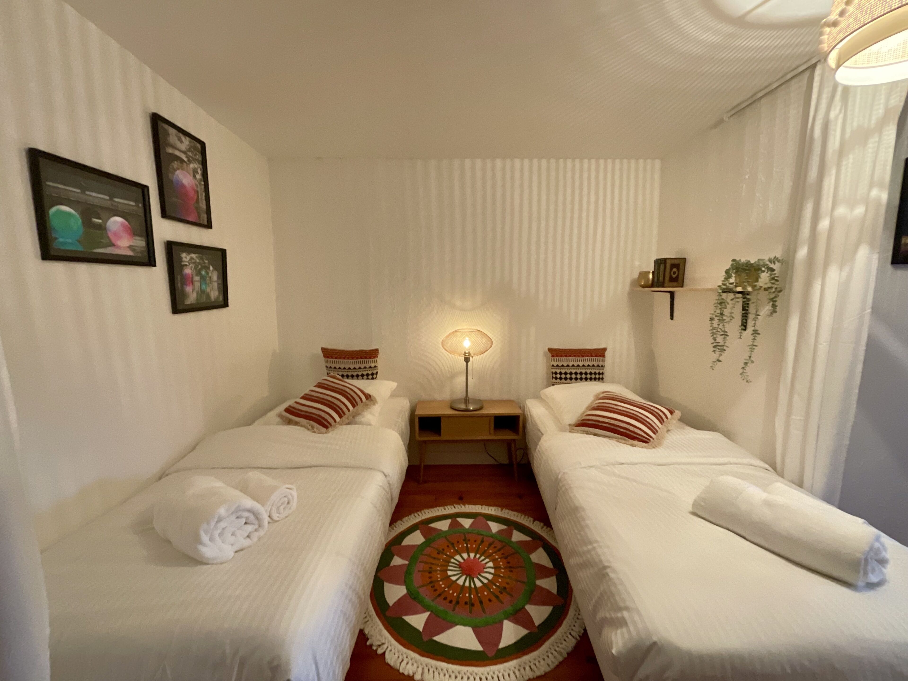 A hotel room with two beds, a round rug, a nightstand with a lamp, and framed pictures on the wall.