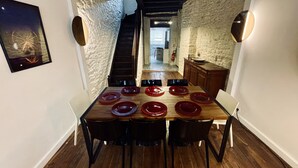 A dining area with a wooden table set for six, flanked by stone walls and a staircase leading to an upper level. - Distinguished Townhouse, "L'Aparté" (Verdun)