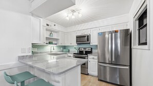 A modern kitchen with white cabinetry, a stainless steel refrigerator, a microwave, and a built-in oven.