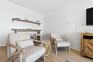 Un salon avec deux fauteuils, une table basse, une cheminée et un téléviseur fixé au mur.