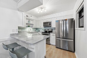 A modern kitchen with white cabinetry, a stainless steel refrigerator, a microwave, and a built-in oven.