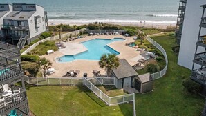 A pool area with two sections, surrounded by a fence, and overlooking the beach.