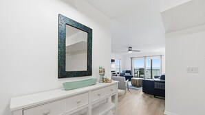A modern living room with a white console table, a large mirror, and a view of the ocean through large windows.