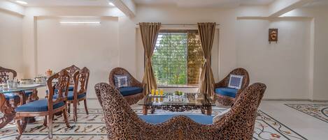Una habitación con una mesa redonda, sillas, un sofá y una ventana con cortinas.