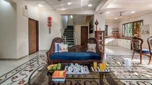 A spacious living room with a sofa, a coffee table with books and fruit, and a kitchen in the background. - CosmicStays Venus Villa- Private pool  (Mawal)
