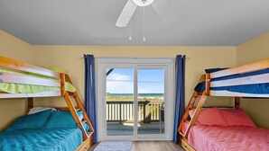 Une chambre avec deux lits superposés, un ventilateur de plafond et une vue sur la plage, accessible par une porte-fenêtre coulissante.