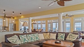 A spacious living room with a sectional sofa, a wooden coffee table, and a view of the ocean through large windows. - 6BR Oceanfront House in North Topsail Beach w Hot Tub, Community Pool, Sleeps 15 (North Topsail Beach)