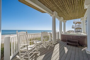 Una terraza de madera con sillas blancas y un jacuzzi con vista a la playa.