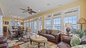 A spacious living room with a large window overlooking the ocean, a dining area with a chandelier, and a ceiling fan. - 6BR Oceanfront House in North Topsail Beach w Hot Tub, Community Pool, Sleeps 15 (North Topsail Beach)