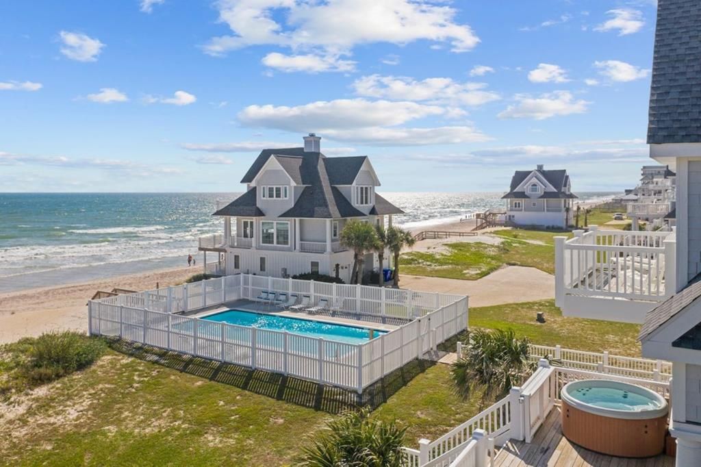 A beachfront property with a swimming pool, a hot tub, and a view of the ocean.