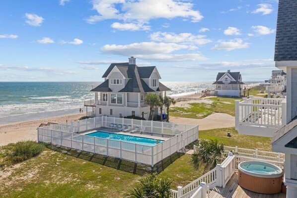 A beachfront property with a swimming pool, a hot tub, and a view of the ocean.