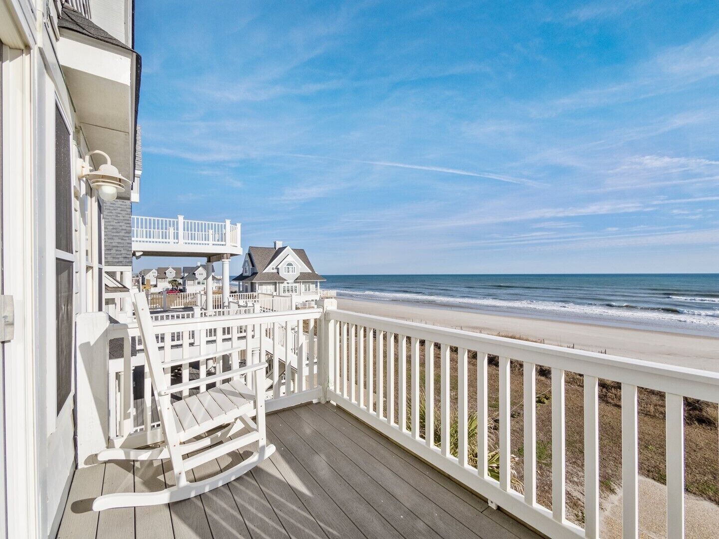 A wooden deck with a white railing overlooking a beach.
