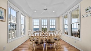 A dining area with a view of the ocean, wooden chairs, and a ceiling fan. - Island Drive 4158 (North Topsail Beach)