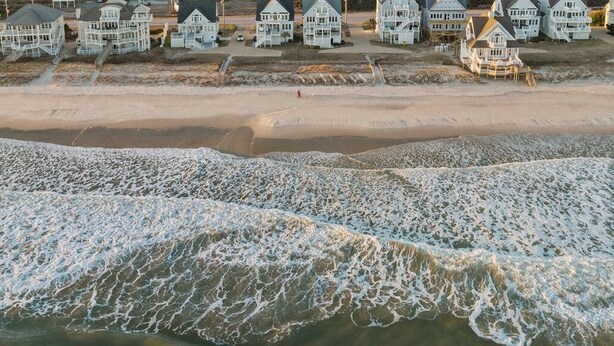 A beachfront property with multiple houses, a sandy beach, and waves crashing onto the shore. - Island Drive 4158 (North Topsail Beach)