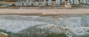 A beachfront property with multiple houses, a sandy beach, and waves crashing onto the shore.