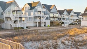 A beachfront property with multiple houses, a wooden staircase leading to a sandy area, and a clear sky. - Island Drive 4158 (North Topsail Beach)