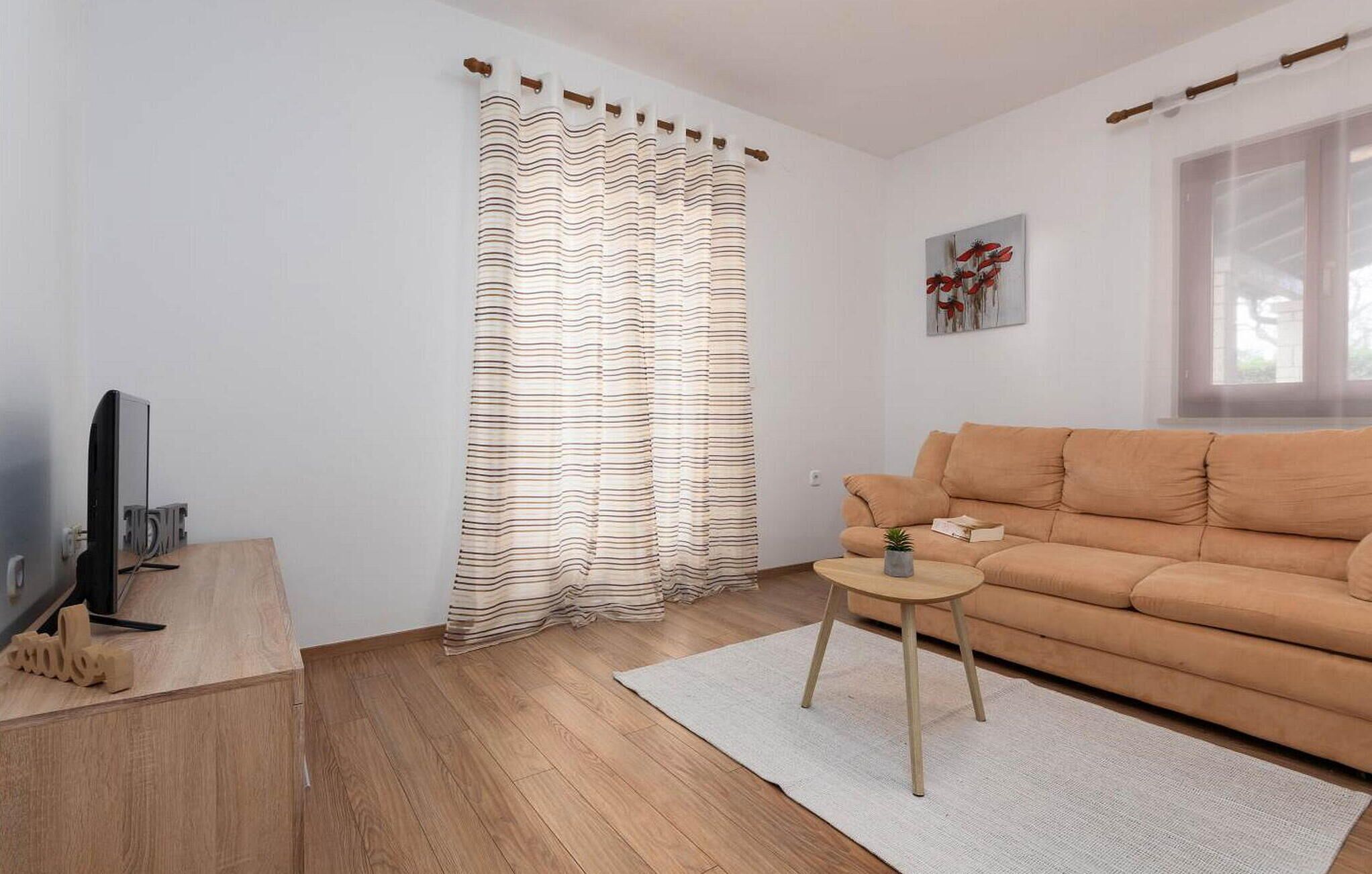 A modern living room with a striped curtain, a beige sofa, a small side table, and a flat-screen TV on a wooden stand.
