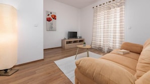 Un salon moderne avec un canapé, un téléviseur posé sur un meuble en bois, une lampe et un tableau accroché au mur.