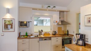 A modern kitchen with white cabinets, a microwave, an oven, a coffee maker, and a window with blinds.