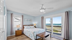 A bedroom with a bed, bedside table, lamp, and a view of the ocean. - A Sassy Siren - 3BR Townhouse on Topsail Island with Ocean and Sound Views (North Topsail Beach)
