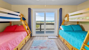 A room with two bunk beds, a ceiling fan, and a view of the beach through a glass door. - A Sassy Siren - 3BR Townhouse on Topsail Island with Ocean and Sound Views (North Topsail Beach)