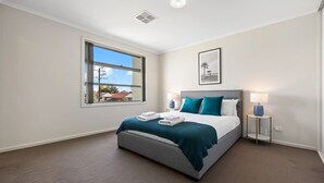 A modern hotel room with a large bed, a window with a view of the outside, a framed picture on the wall, and a bedside table with a lamp. - The Charming Living 3BR Townhouse/Perfect Vacation (Largs North)