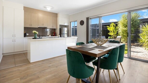 A modern kitchen with white cabinets, a central island, and a dining area with green chairs. - The Charming Living 3BR Townhouse/Perfect Vacation (Largs North)